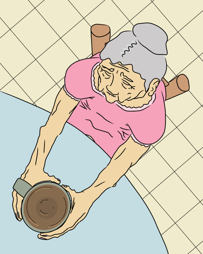 An overhead shot of an old woman sitting at a table, holding a tea mug