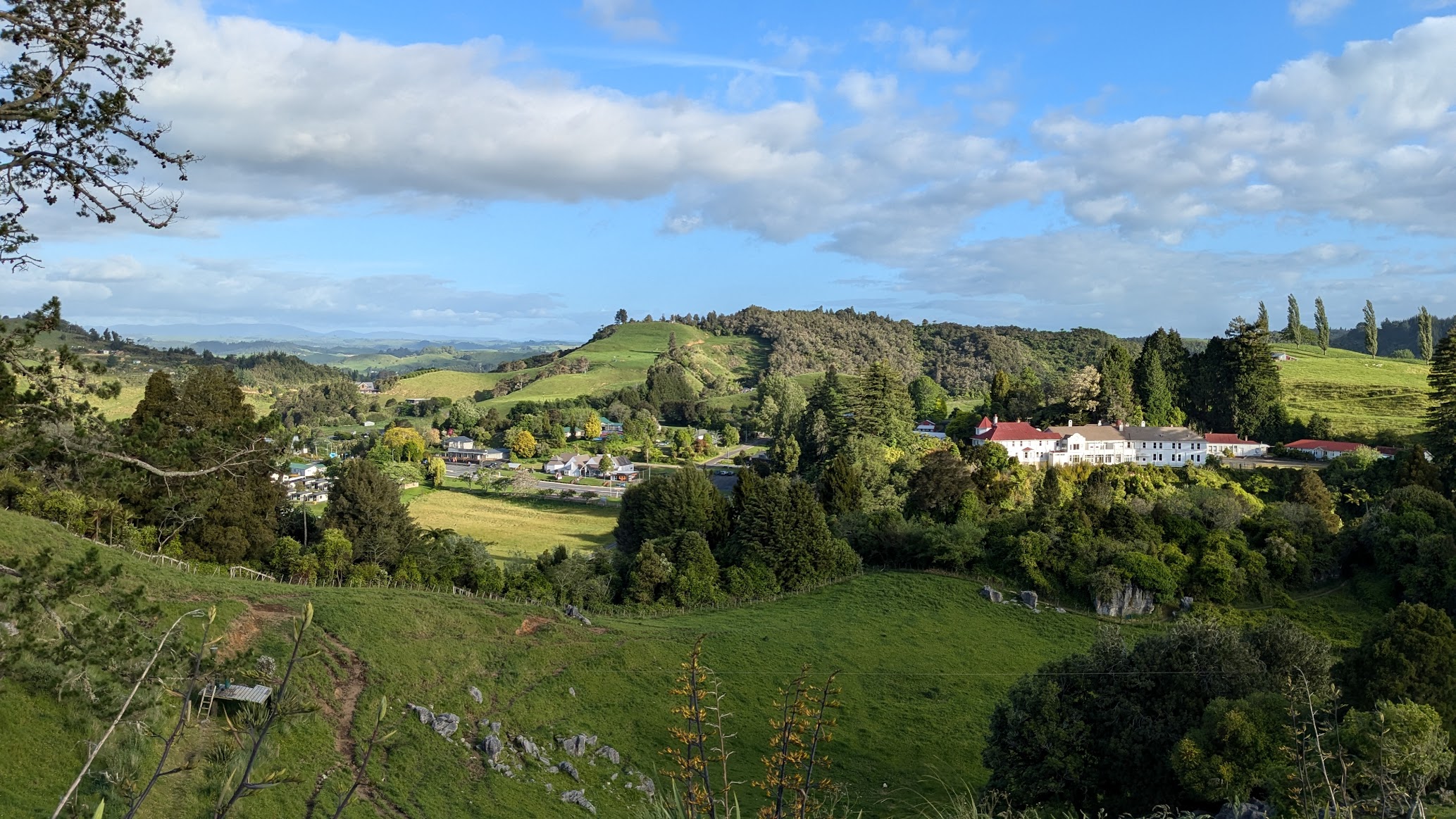 A photo I took of the New Zealand countryside with rolling green hills and The Waitomo Caves Hotel, where Queen Elizabeth II stayed in when she visited