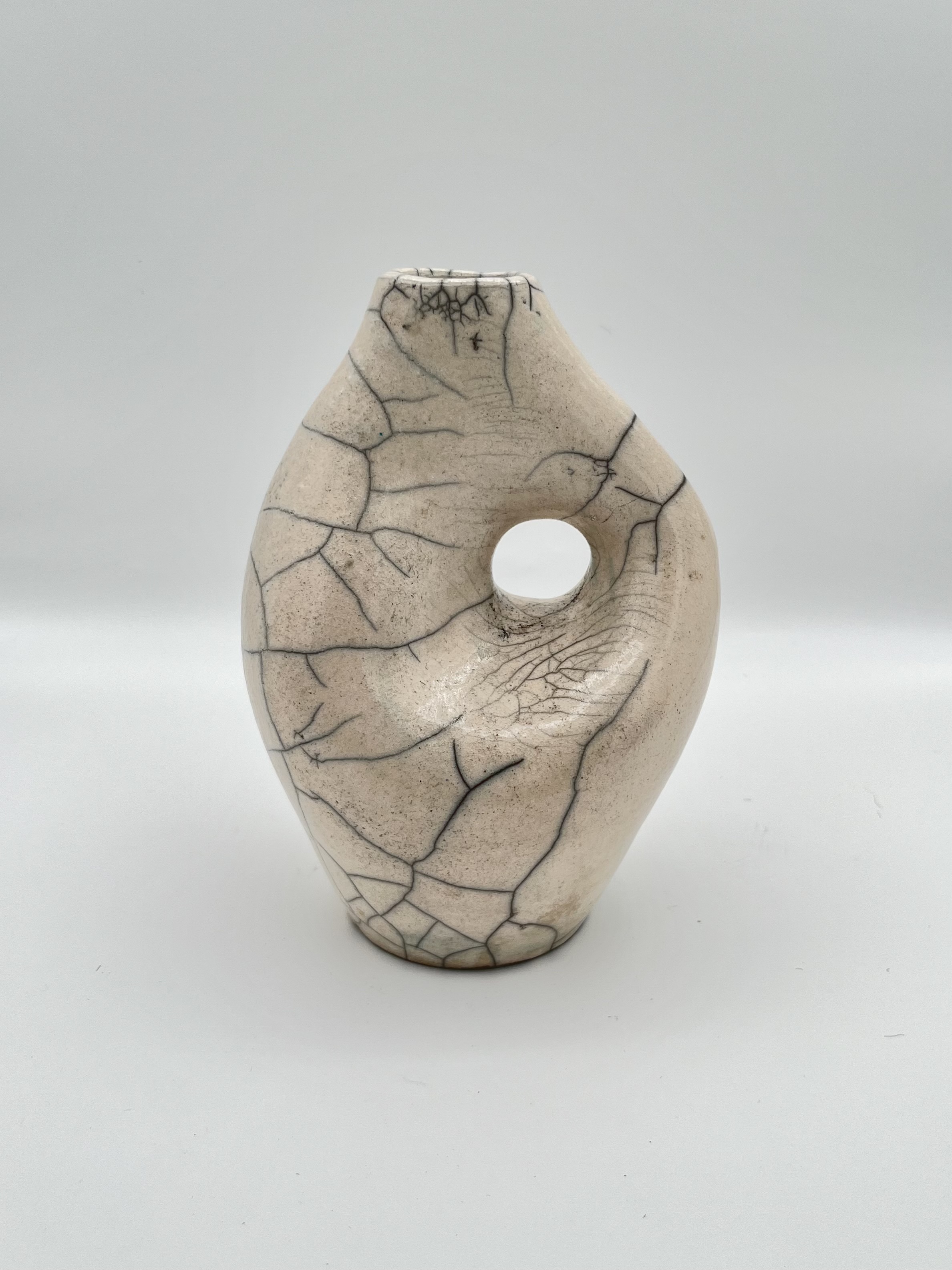 A bright lightbox photo of a curved, glossy white sculpture with a hole through it in the middle that has thin black cracks framing the hole on all sides