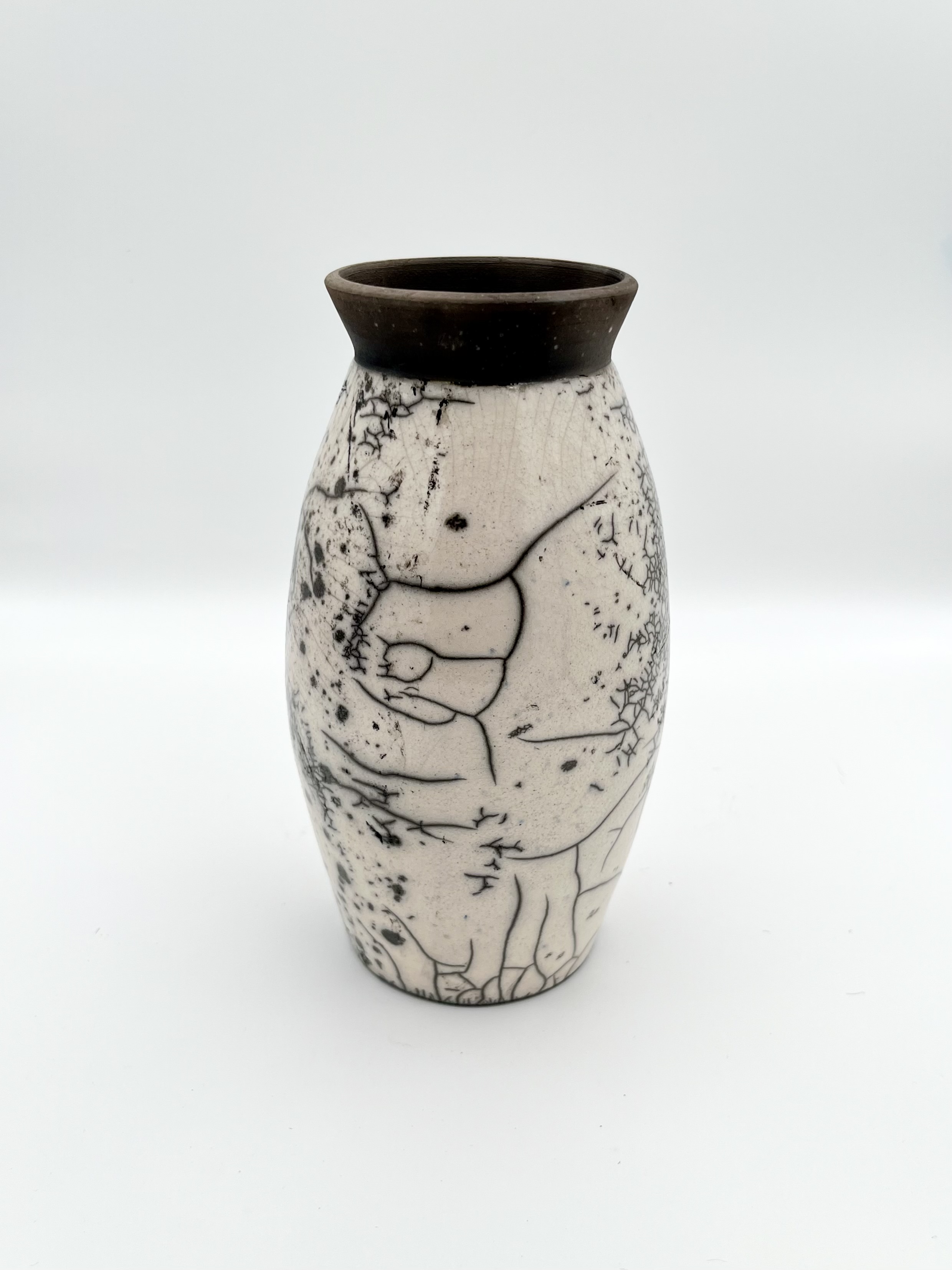 A glossy white vase curved like parentheses has a solid matte black lip at the top and is covered with black cracks of varying sizes all over the rest of the body
