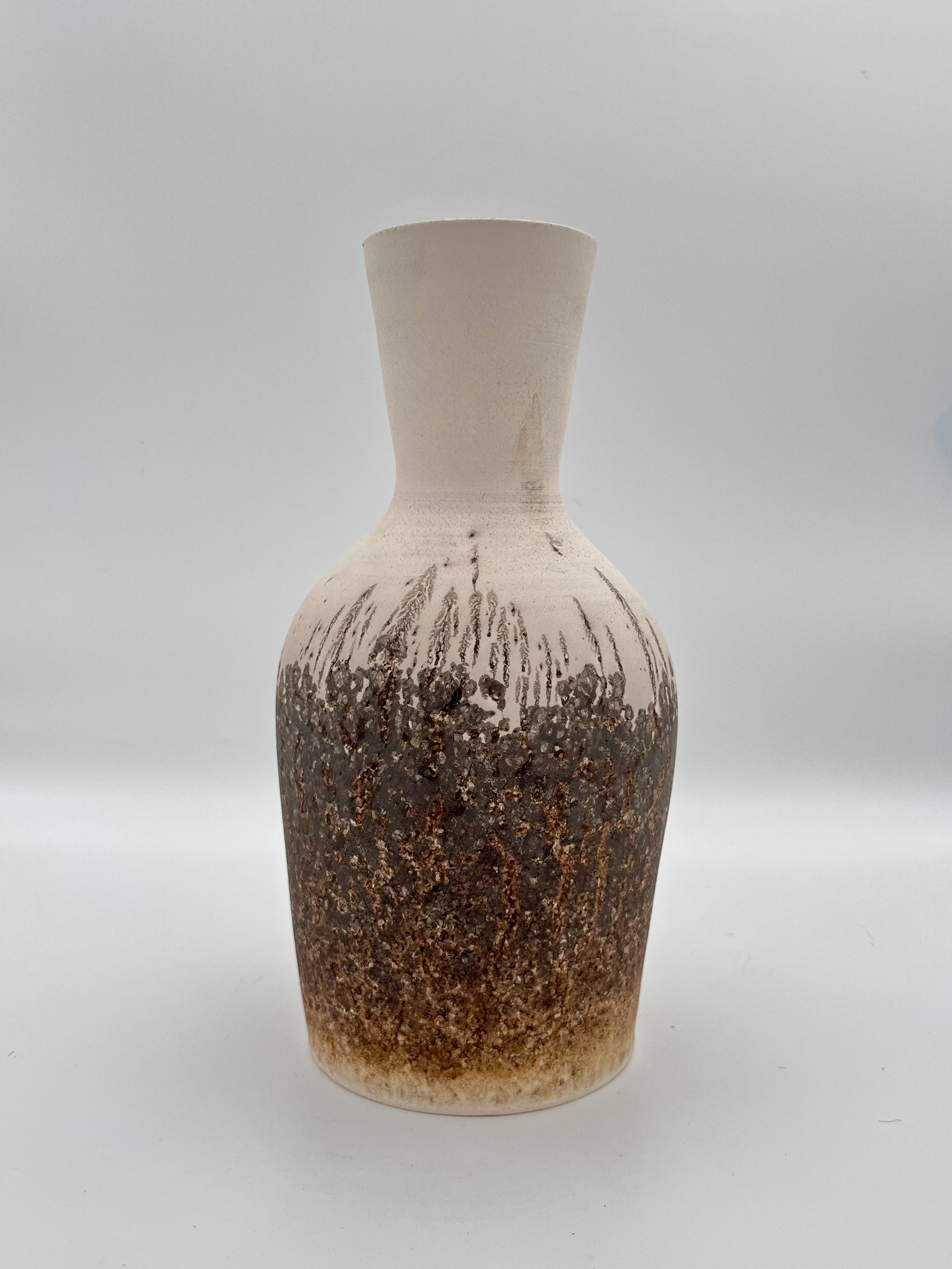 A white flared bottle vase with a burnt brown bottom-half from where the obvara mixture bubbled up and fused onto the vase wall