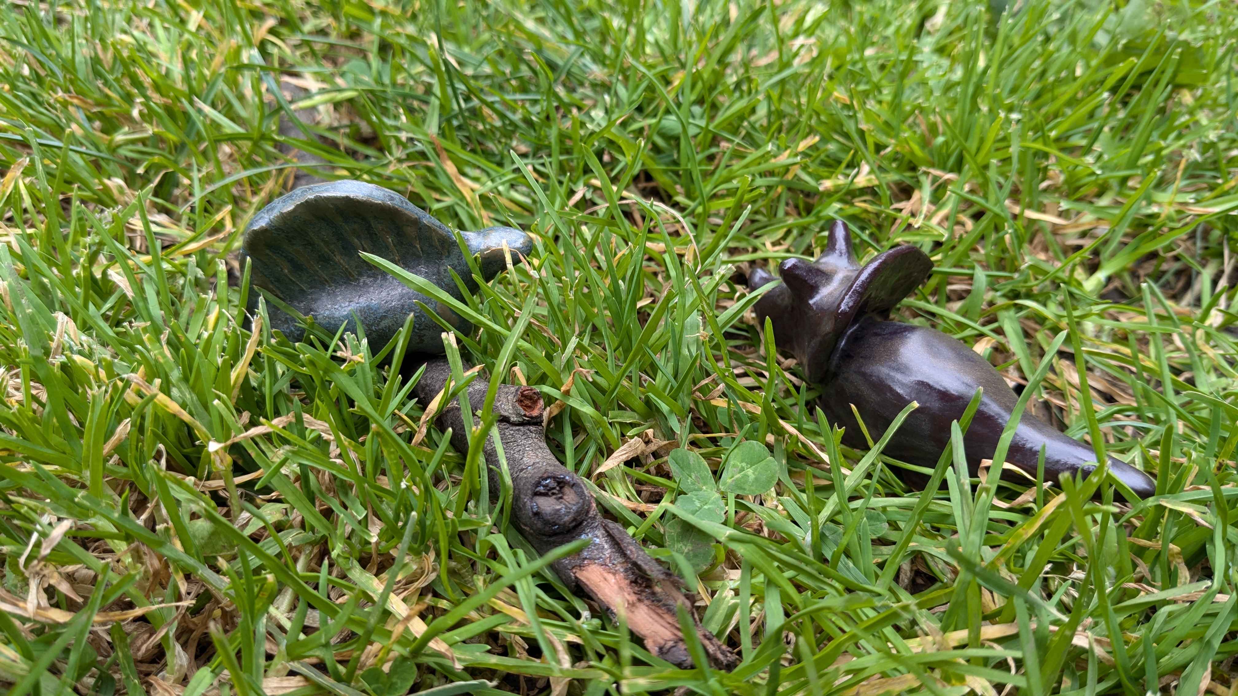 A low-angle shot in the grass of a green dimetrodon resting on a stick on the left and a brown triceratops on the right.