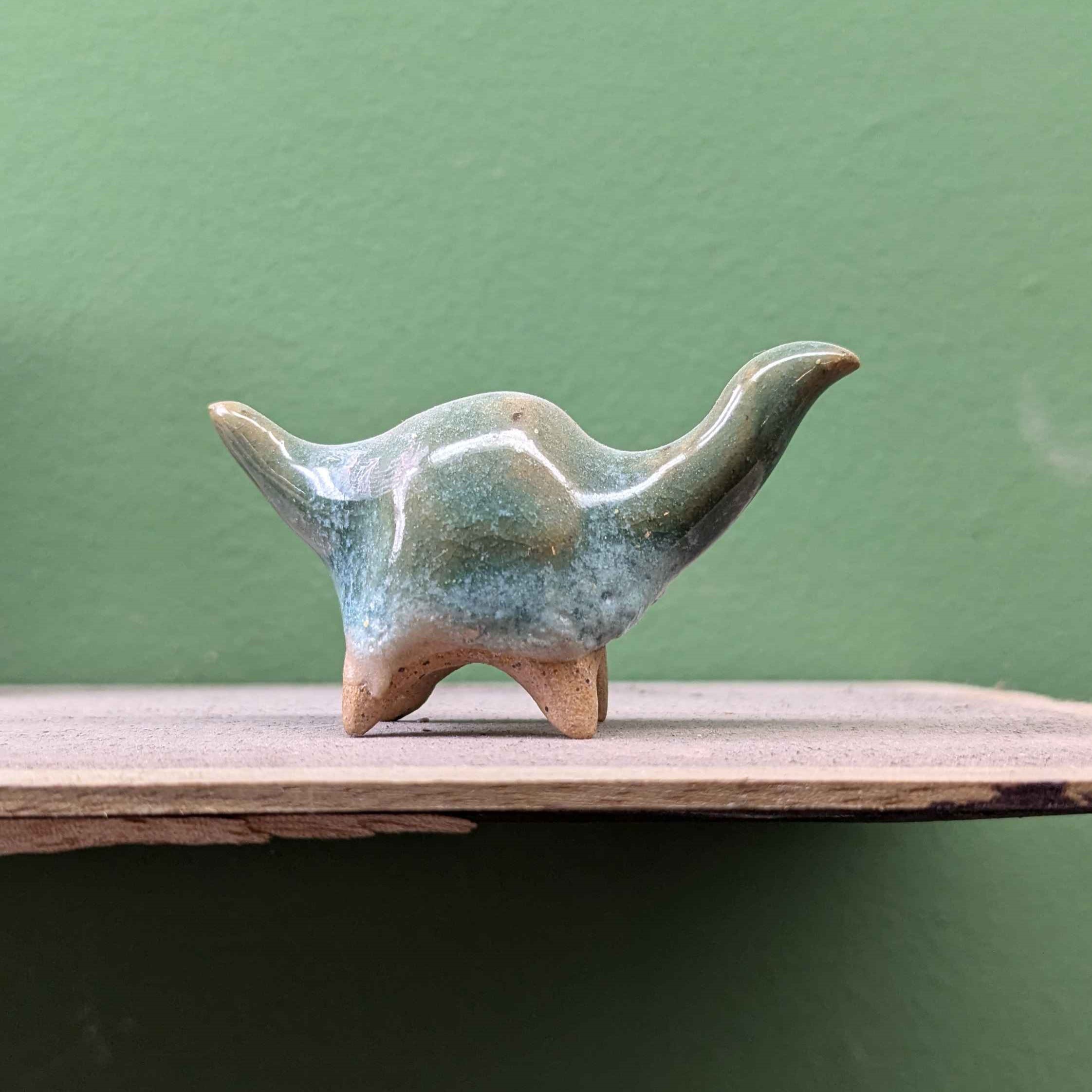 A ceramic brontosaurus someone else made with a large orb-like center and green and crackling blue highlight glaze over a speckled body